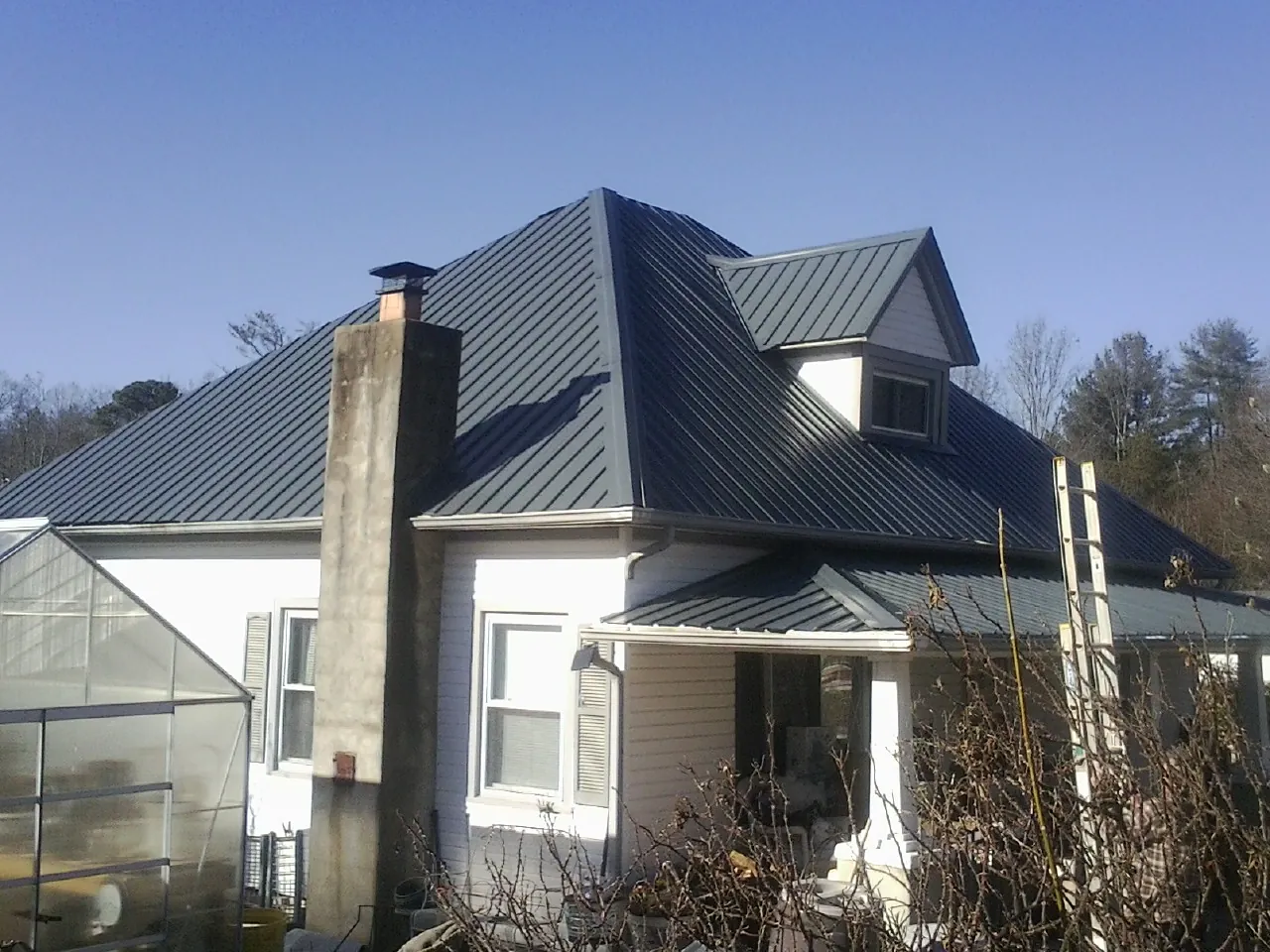 Dark blue standing seam metal roof on a white farmhouse with dormer — Slate & Tile Roof Repair by Roofing Brothers in Niagara Falls