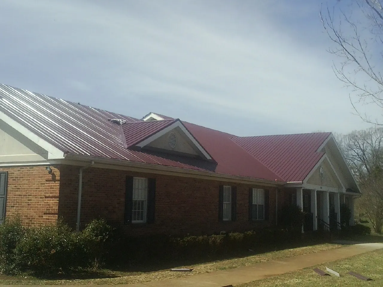 Red metal roof with gabled entries on a long brick building, from a Hail Damage Roof Repair job in Niagara Falls