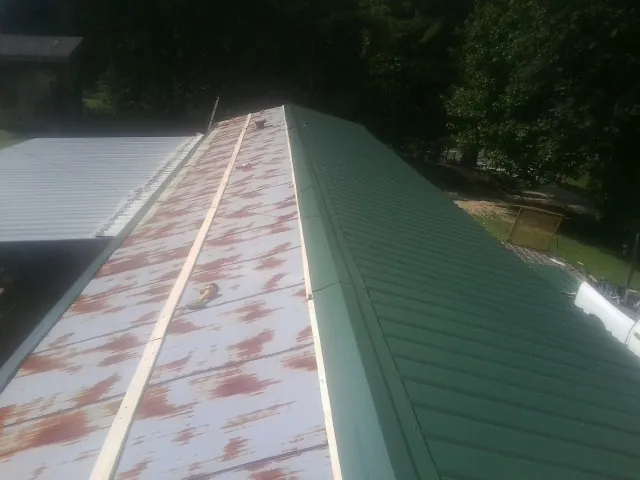 Old rusted panels beside newly installed green metal roofing — Wind Damage Roof Repair by Roofing Brothers in Niagara Falls