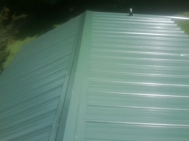 New green metal panels meeting at the ridge of a roof — Flat Roof Repair work by our crew in Niagara Falls