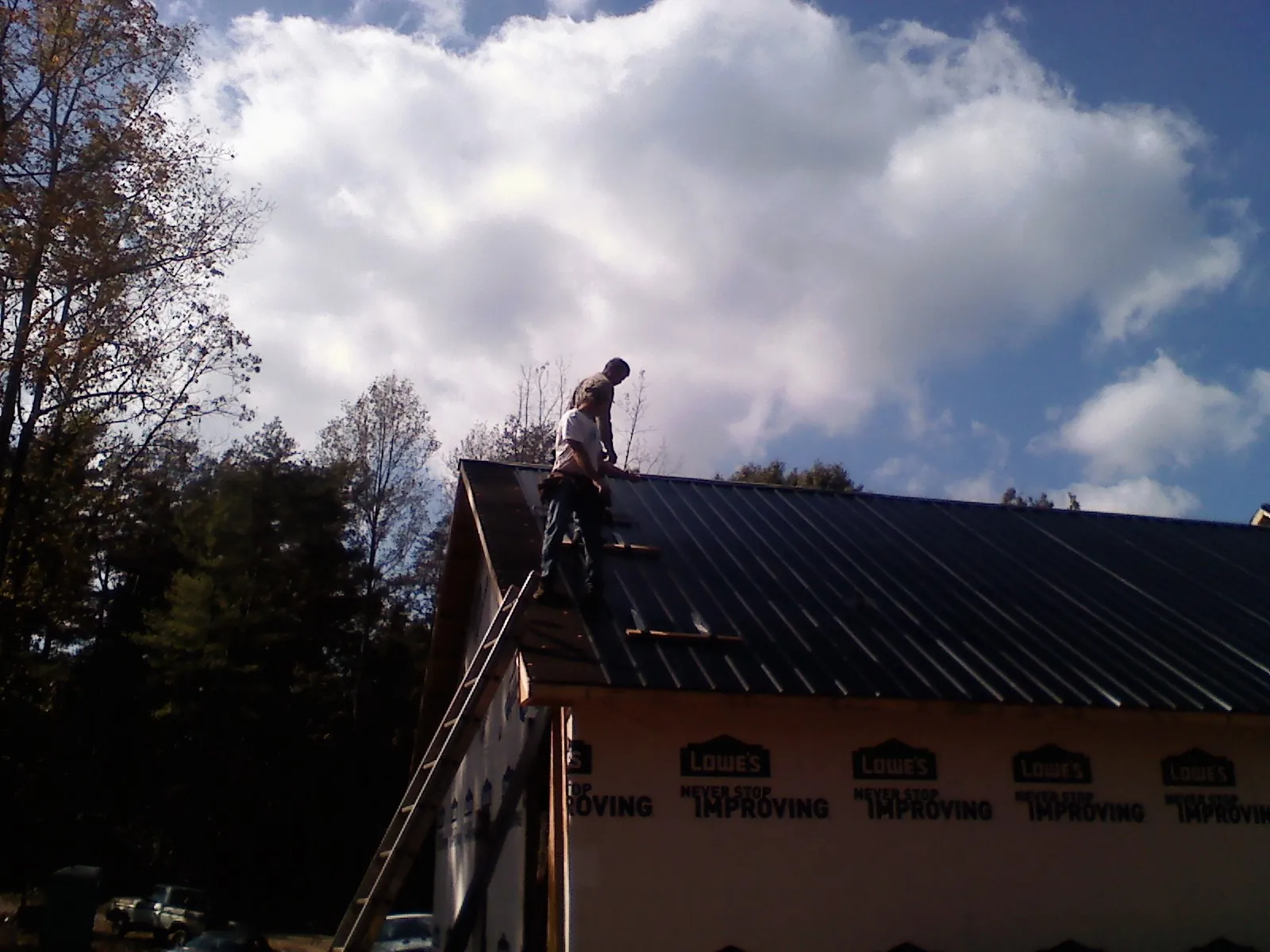 Roofer fastening dark metal panels high against a cloudy sky in Niagara Falls