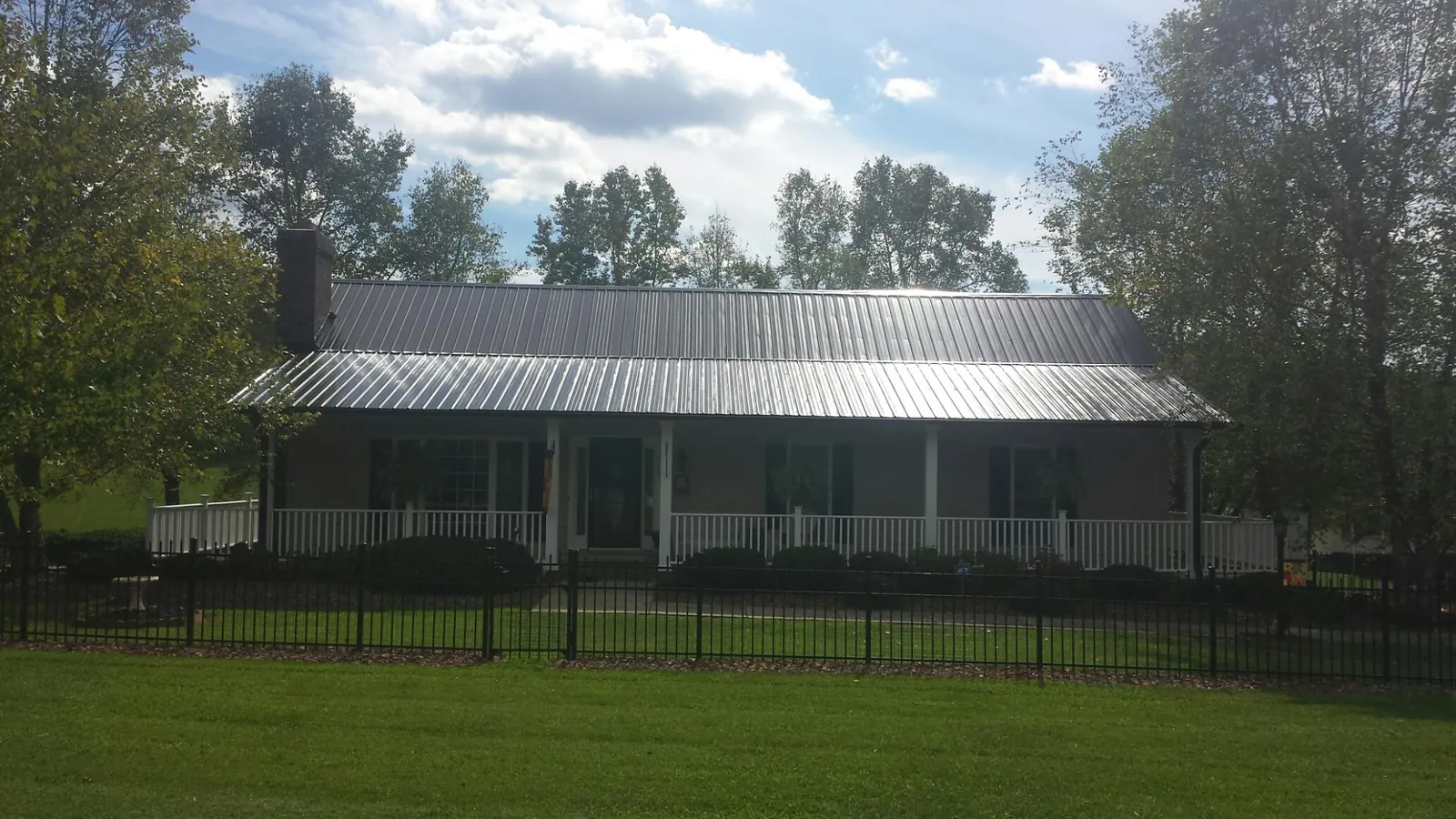 Gray metal roof on a brick ranch with a full width front porch — Gutter Guard Installation work by our crew in Niagara Falls