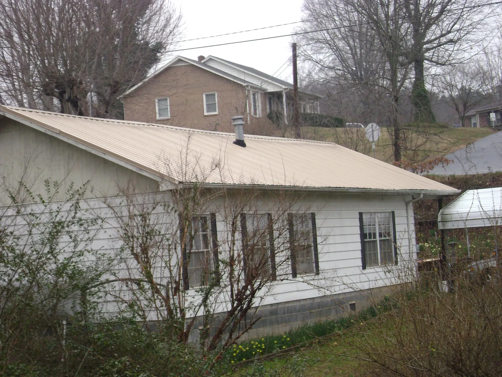 Tan metal roof on a white sided house set into a hillside — Commercial Roofing by Roofing Brothers in Niagara Falls