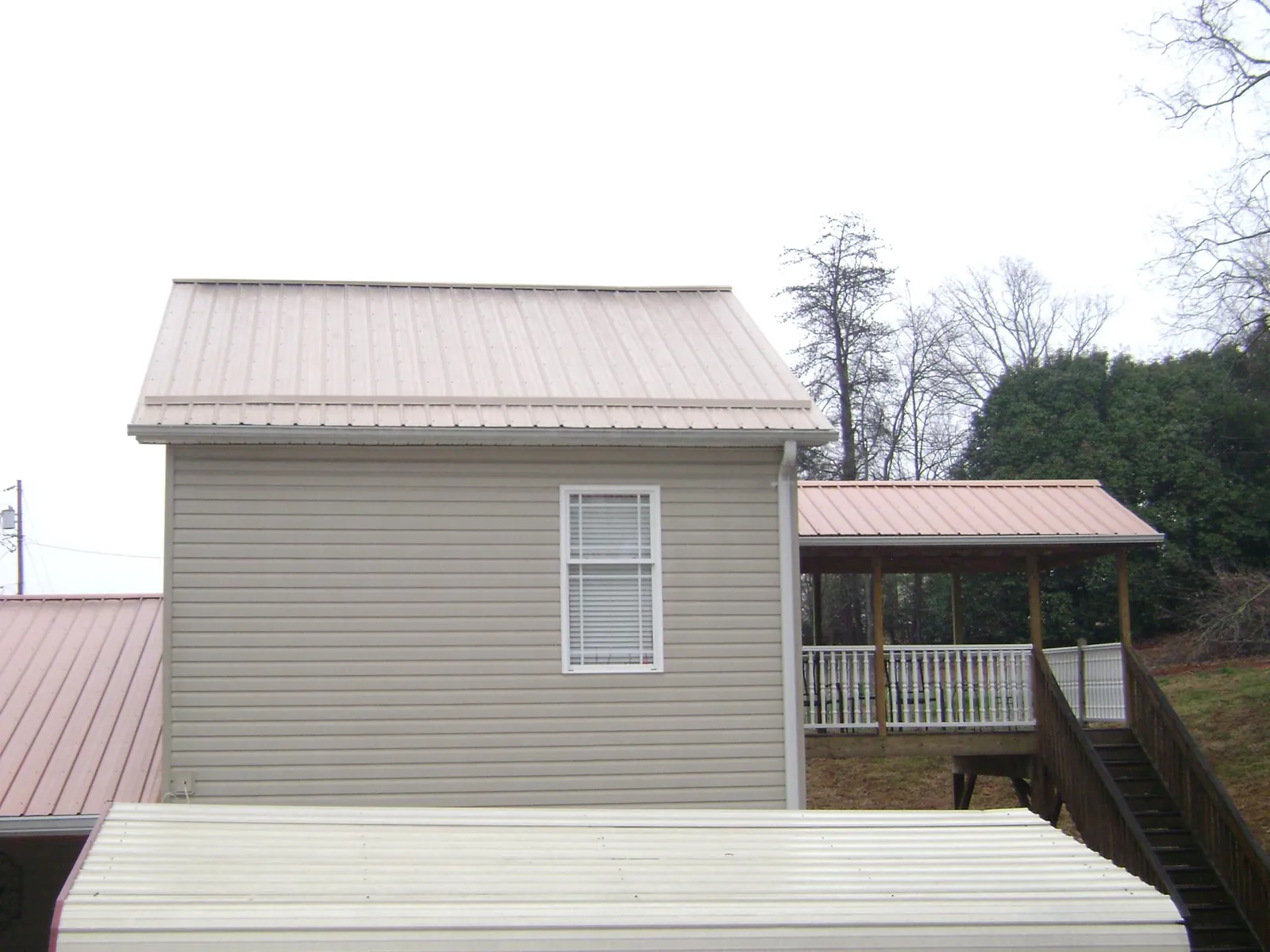 Tan metal roofs on a two story addition and attached porch, from a Roof Replacement job in Niagara Falls